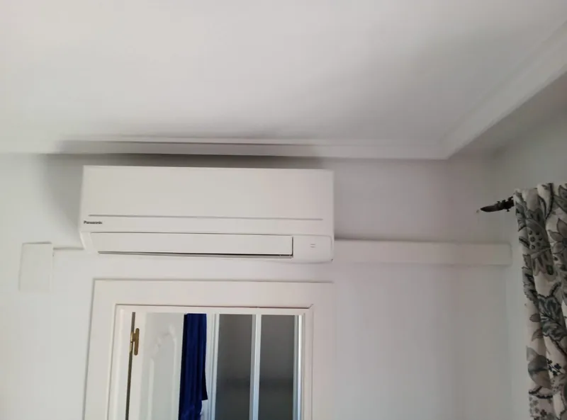 Aire acondicionado split Panasonic instalado sobre la puerta de un dormitorio, con la canaleta integrada en la moldura