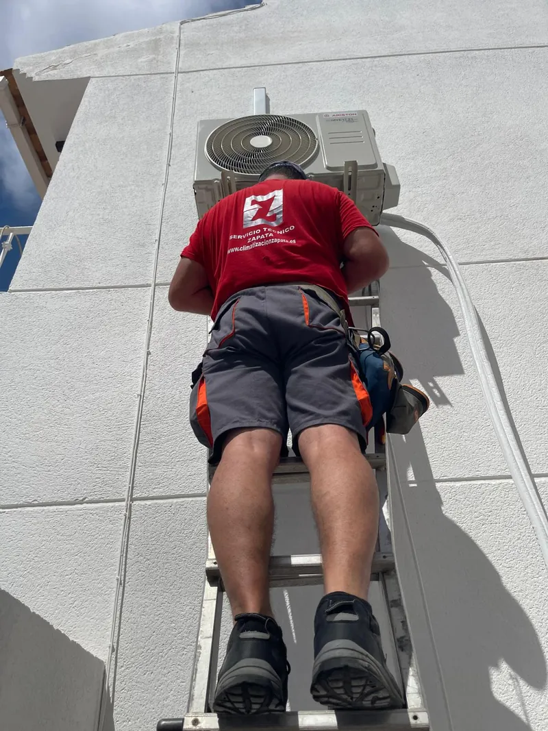 Técnico de Climatización Zapata revisando la unidad exterior de un aire acondicionado en fachada